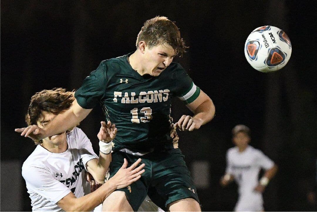 A Saint Stephen's Falcons soccer player heads the ball during a night match.