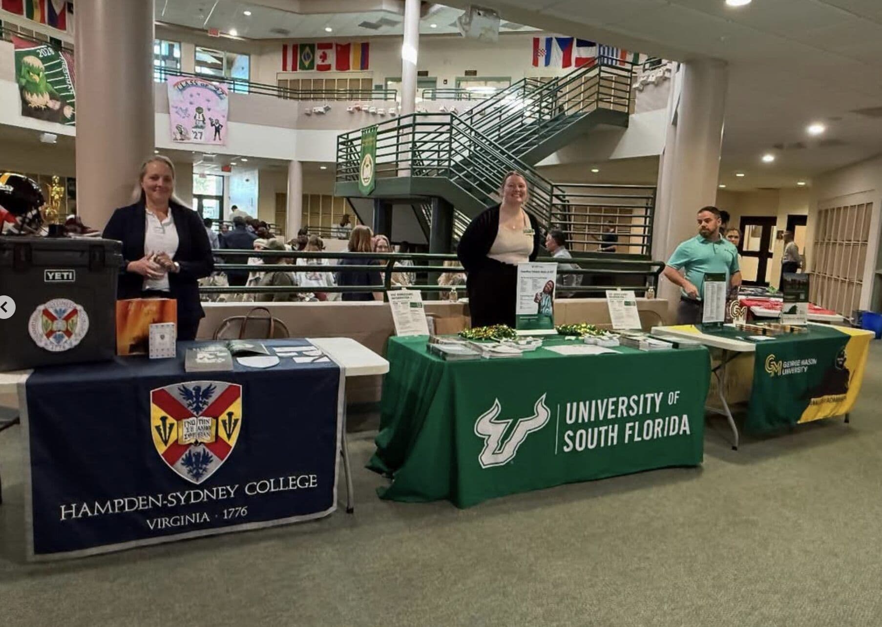 College representatives staff tables at a college fair in the campus hall.
