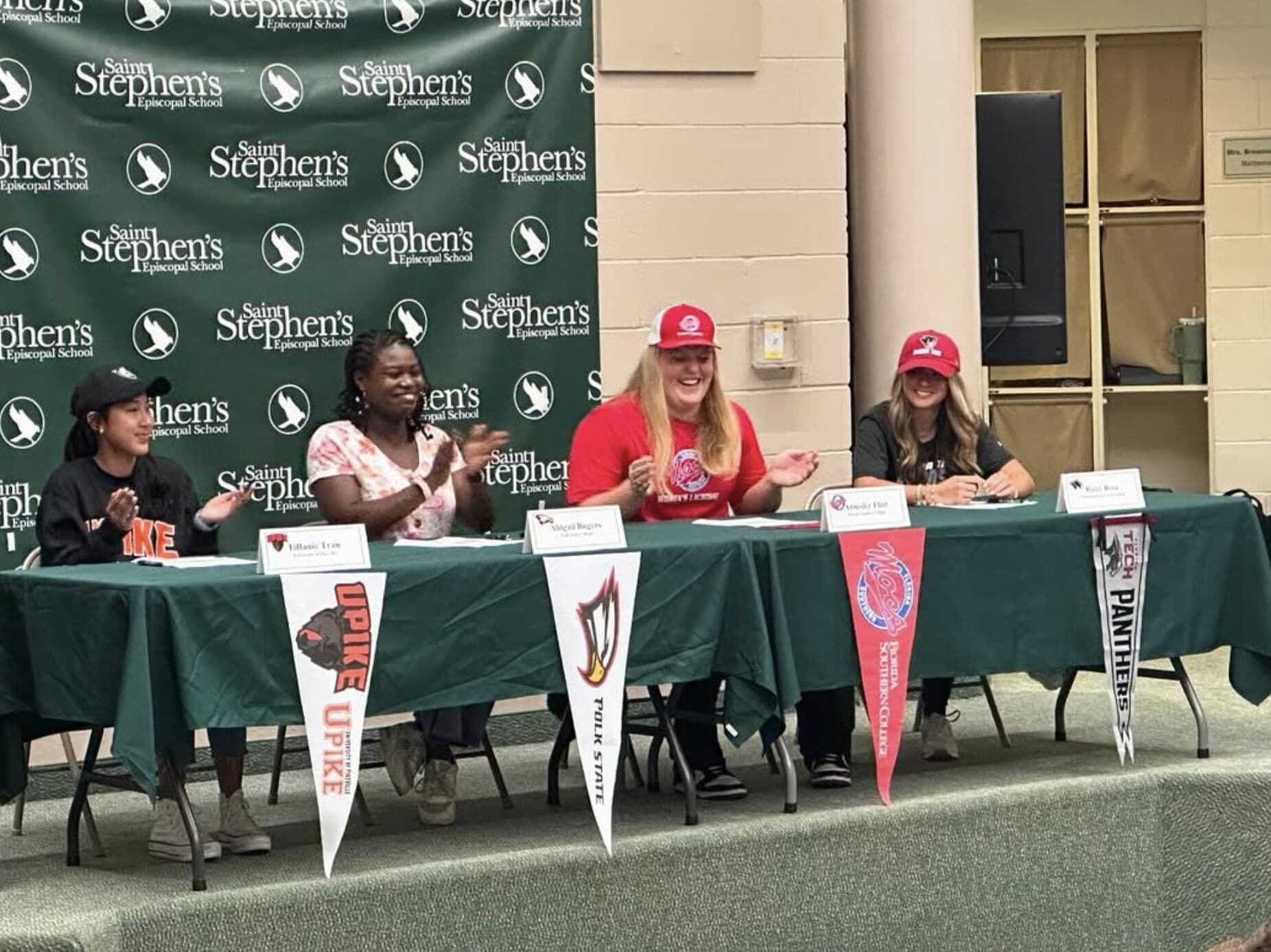 Student-athletes sign with their colleges at a table lined with college pennants.