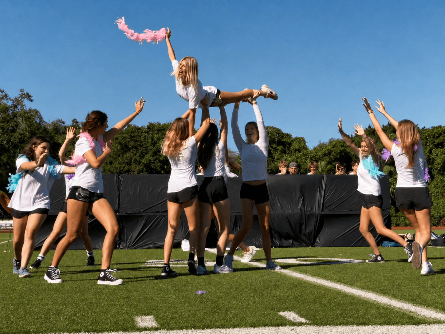 Upper School students celebrating at a homecoming pep rally, lifting a classmate on the field